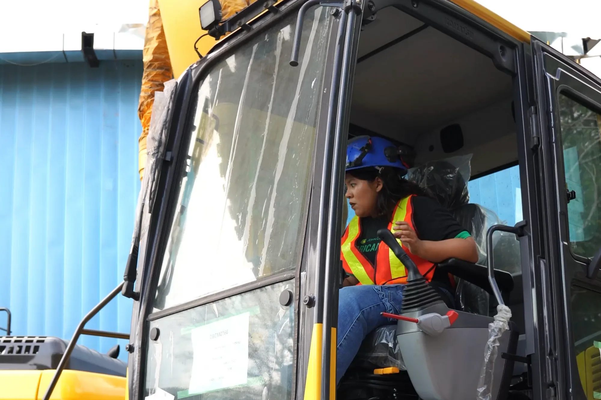 Trainee with hard hat and vest in the cab of a hydraulic excavator during practice