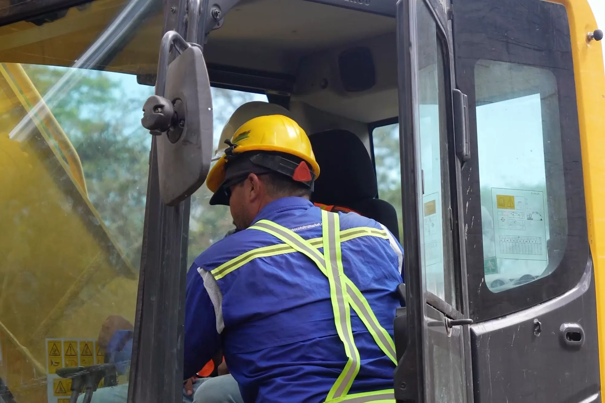 Instructor en la puerta de la cabina de una excavadora dando indicaciones al alumno que la opera