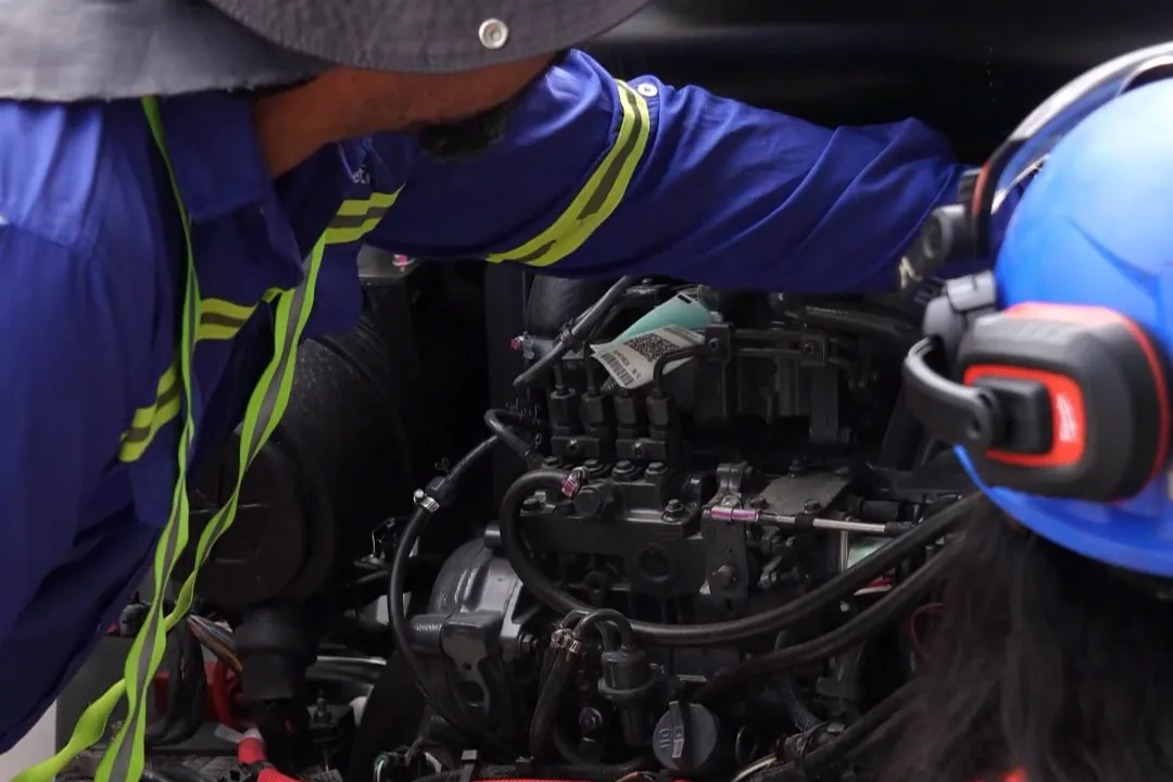 Instructor showing a trainee a skid steer loader's engine compartment during the pre-operation inspection